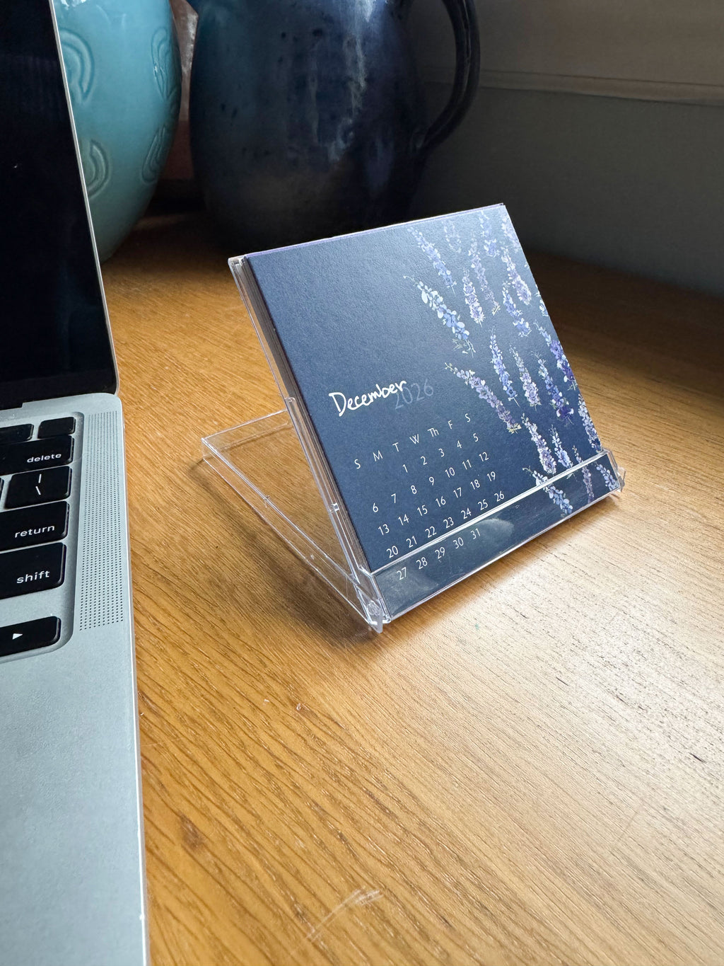 Calendar on a stand next to a laptop on a wooden surface