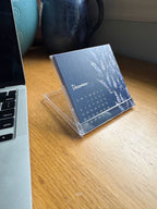 Calendar on a stand next to a laptop on a wooden surface