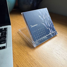 Calendar on a stand next to a laptop on a wooden surface