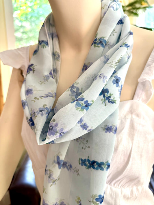 Person wearing a floral scarf with delphinium blue flowers on a blurred background