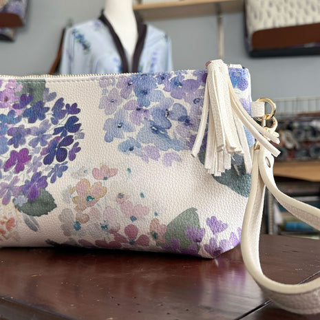 Floral-patterned pouch with a white strap on a wooden surface