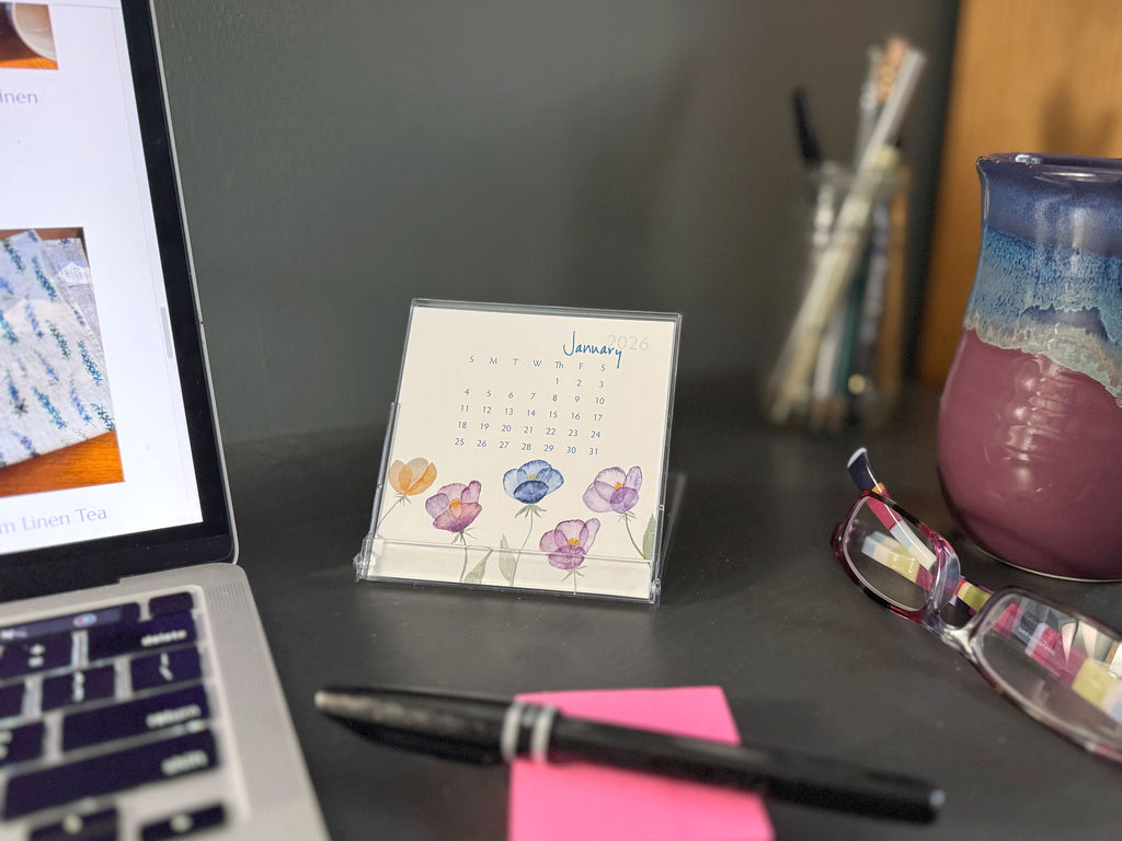 Desk setup with a laptop, calendar, pen, and glasses on a dark surface.