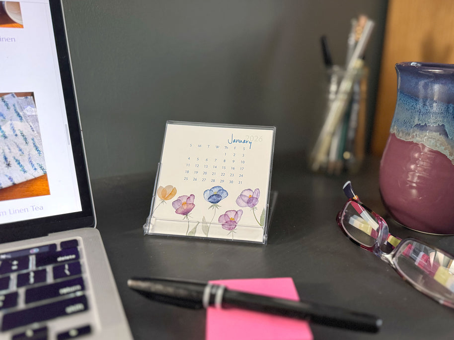 Desk setup with a laptop, calendar, pen, and glasses on a dark surface.